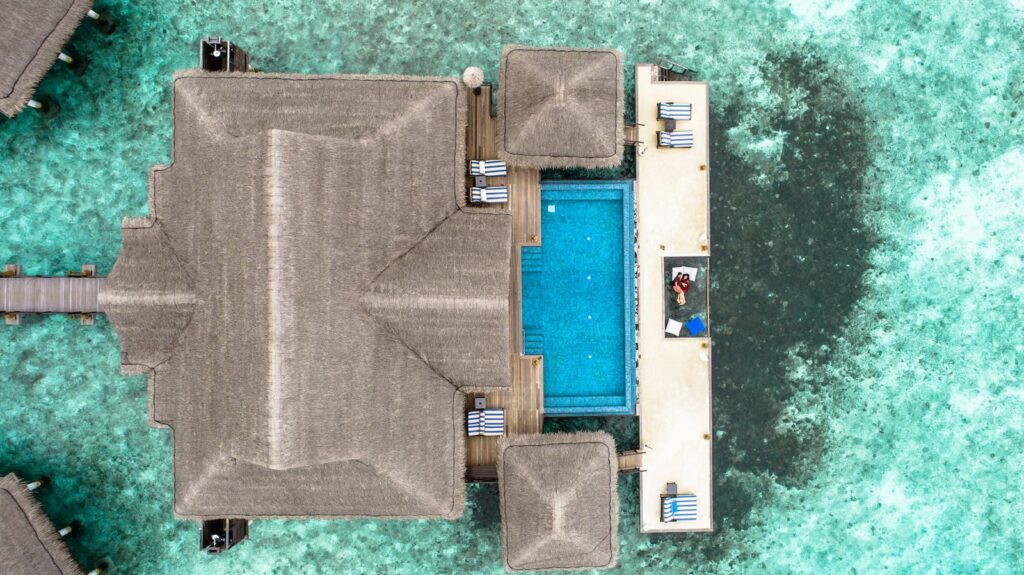 Stunning aerial view of a luxury villa with a swimming pool in the Maldives over turquoise waters.